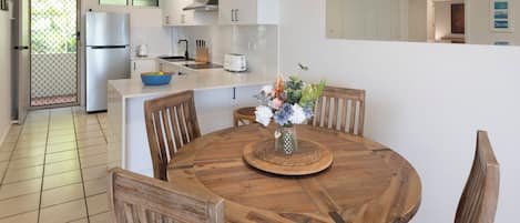 A modern kitchen with white cabinetry, a built-in oven, and a dining area with a wooden table and chairs.