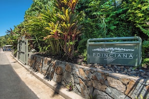 A sign for 'Poinciana Lodge' with a stone wall and tropical plants.