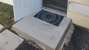 Una habitación con cama, una puerta y un pequeño espacio al aire libre con un felpudo.