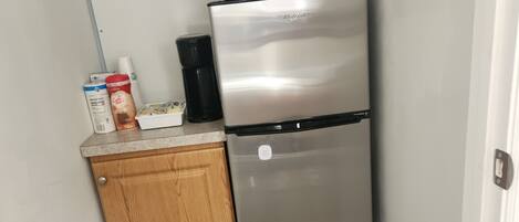 A compact kitchen with a stainless steel refrigerator, a microwave, and a wooden cabinet.