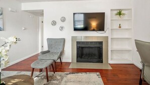 A living room with a fireplace, a television mounted above it, and a plant on a shelf.