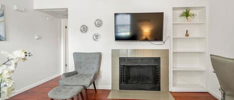 A living room with a fireplace, a television mounted above it, and a plant on a shelf.