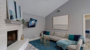 A living room with a fireplace, a sofa, a coffee table, and a TV mounted on the wall. - Modern Comfort Lux Stay | Near DFW Airport (Euless)
