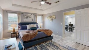 A bedroom with a bed, a ceiling fan, a window with blinds, and a door leading to another room. - Modern Comfort Lux Stay | Near DFW Airport (Euless)