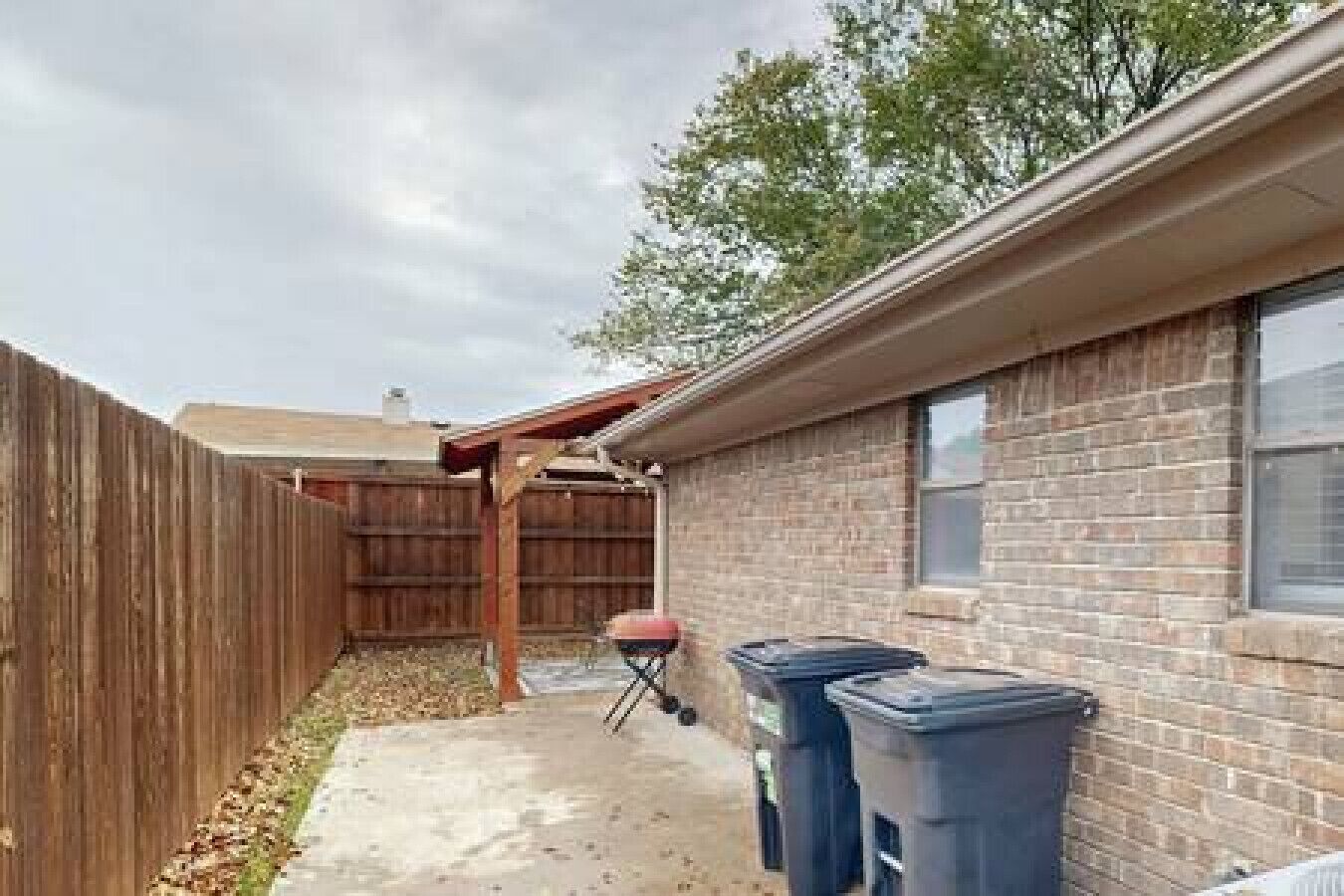 A backyard with a wooden fence, a brick wall, and a covered patio area.