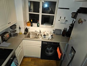 Ett kompakt kök med diskmaskin, diskho, fönster och tvättmaskin.