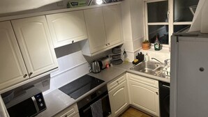 Cocina pequeña con gabinetes blancos, estufa negra, lavamanos y refrigerador.