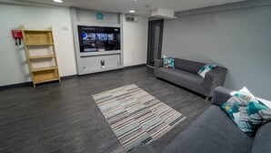 A modern living room with a grey sofa, a wooden shelf, a flat-screen TV, and a patterned rug. - Captivating 1-Bed studio in Birmingham (Birmingham)