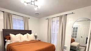 Une chambre à coucher avec un grand lit, une table de chevet, un miroir et une fenêtre avec des rideaux.