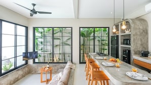 Una cocina moderna con una isla central, ventanas amplias con vegetación y un ventilador de techo.