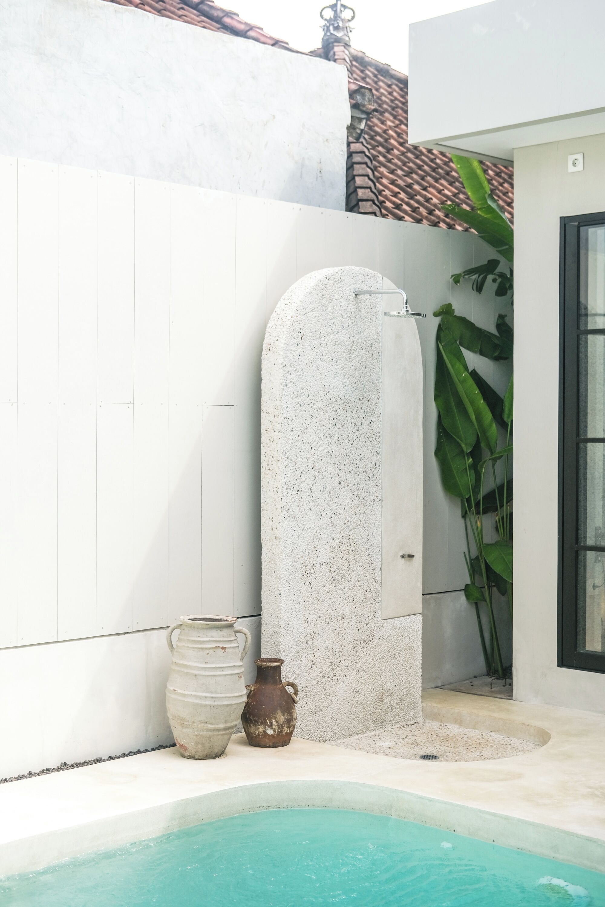 A pool area with a white tiled wall, a concrete structure, and two pots.