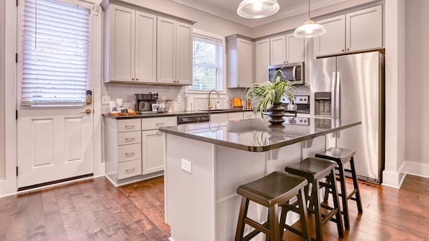 A modern kitchen with white cabinets, a central island with stools, stainless steel appliances, and a pendant light.