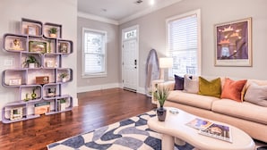 A living room with a beige sofa, a coffee table, and a bookshelf with decorative items.