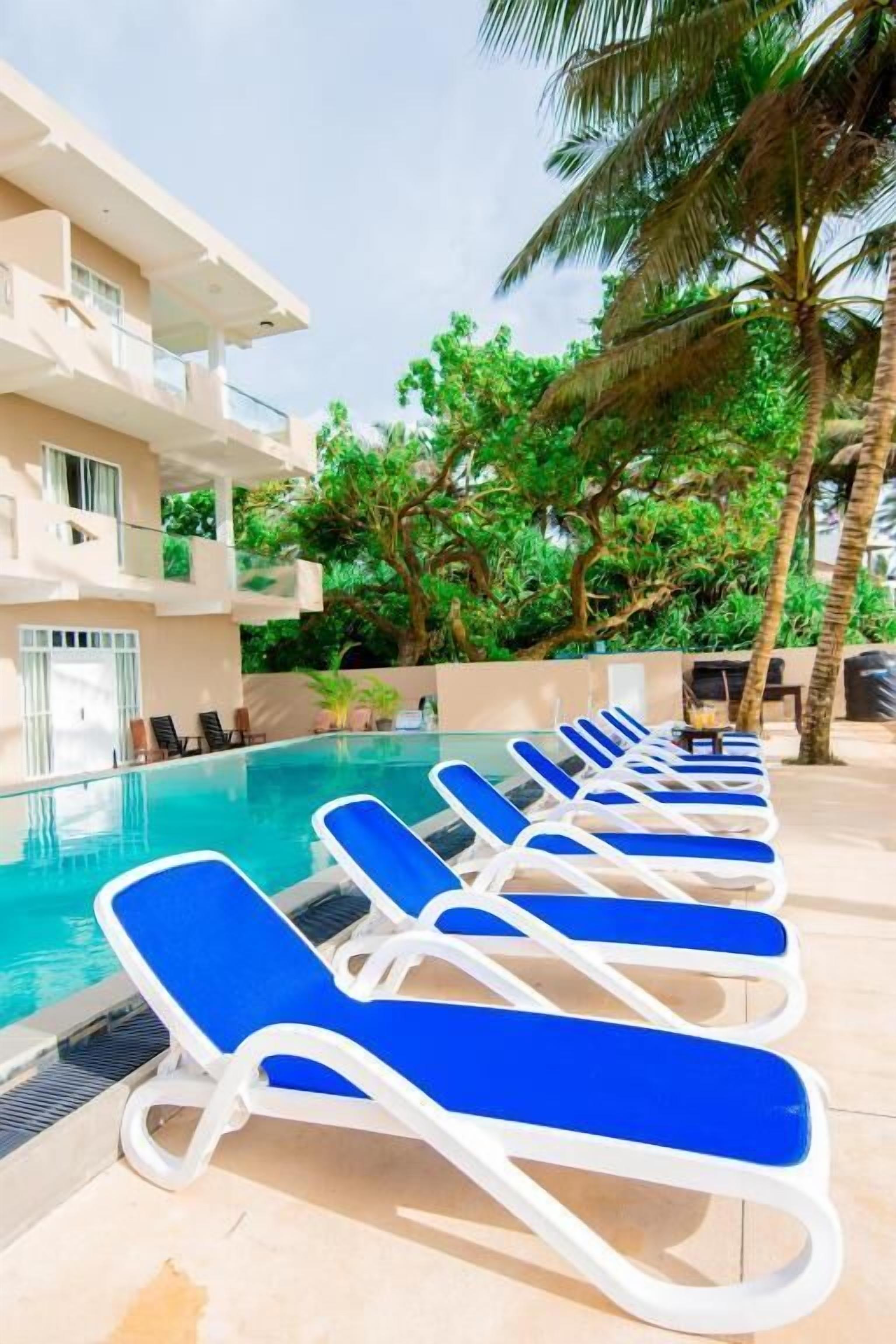 Uma área à beira da piscina com espreguiçadeiras e um edifício com varandas.
