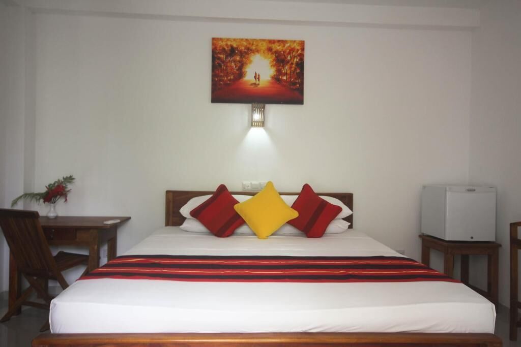 A hotel room with a bed, a desk, a chair, a TV, and a painting on the wall.
