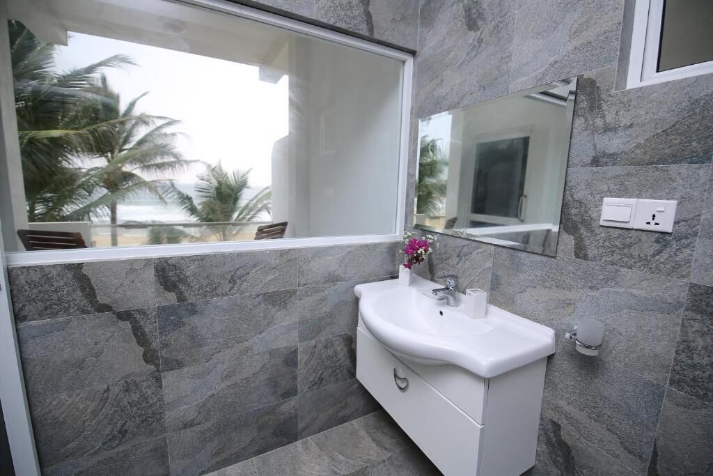 A bathroom with a white sink, a mirror, and a view of palm trees outside.