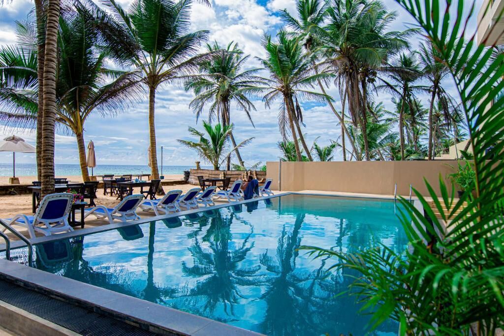 A pool area with lounge chairs and palm trees, overlooking a beach.