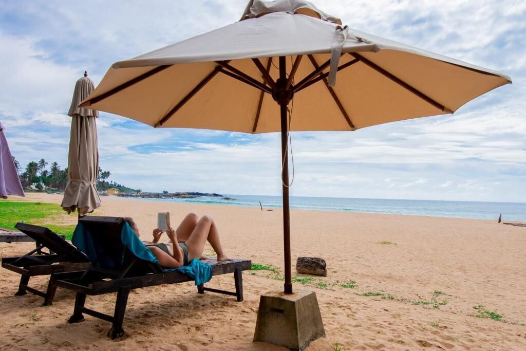 A beach with a lounge chair and a large umbrella providing shade.
