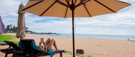 A beach with a lounge chair and a large umbrella providing shade.