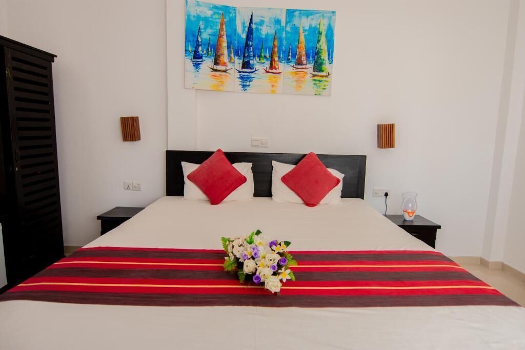 Camera d'albergo con un letto, cuscini rossi e bianchi, un'interpretazione floreale e un quadro con dei velieri sulla parete.