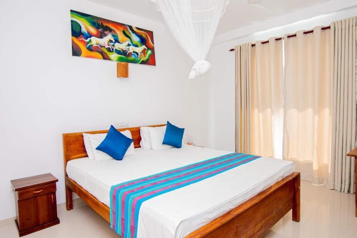 A neatly made bed with a striped blanket, a bedside table, and a colorful abstract painting on the wall.