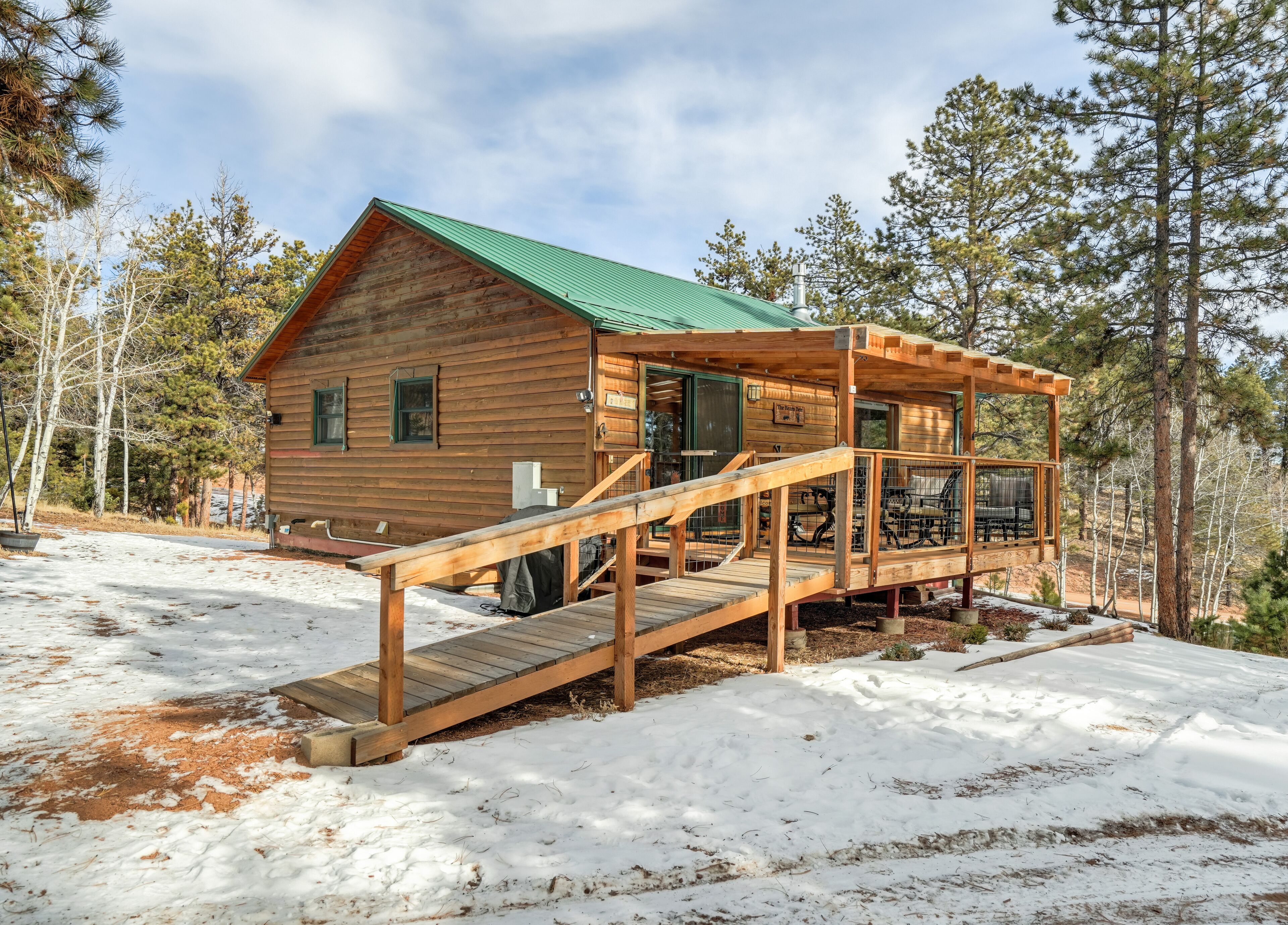 A wooden cabin with a green roof, a covered porch, and a staircase leading to the entrance.