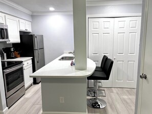 A kitchen with white cabinets, a stainless steel refrigerator, and a black countertop. - I44 - Apt|Patio|11mi to Convention Ctr|Sleeps 2 (Irving)