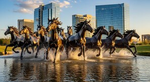 A group of bronze horse statues in motion, set against a backdrop of modern buildings and a clear sky.