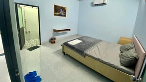 A bedroom with a bed, a wall-mounted air conditioner, a small shelf, and a fan. - ĐOAN GIA (Dong Xoai)