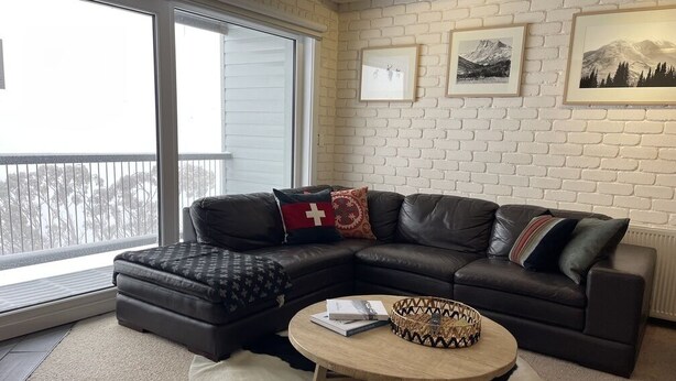 A living room with a leather sectional sofa, a round coffee table, and a large window.