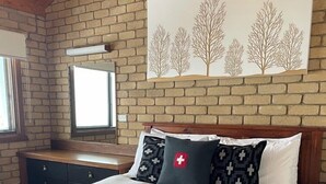 A bedroom with a wooden headboard, a bed with white bedding, patterned pillows, a blanket, and a wall-mounted picture of trees.