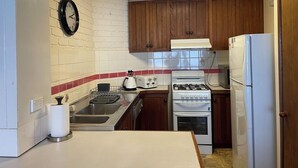 A compact kitchen with wooden cabinets, a gas stove, a white refrigerator, and a tiled backsplash.