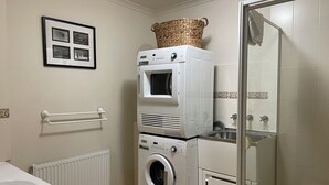 A laundry room with stacked appliances, a radiator, a framed picture, and a shower area.