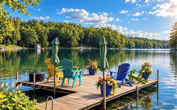 A wooden dock with chairs and umbrellas, overlooking a calm lake with trees in the background.