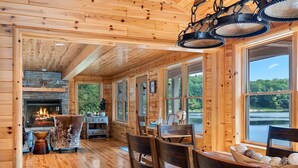 A cozy cabin interior with wooden walls, a fireplace, and large windows offering a view of the outdoors.