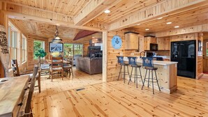 A wooden cabin interior with a dining area, kitchen, and bar.