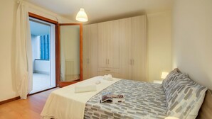 Un dormitorio con cama, mesita de noche, armario y puerta corrediza de vidrio que da a un espacio exterior.