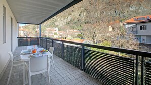 Un balcón con una mesa lista para comer, una silla y vistas a un paisaje montañoso.