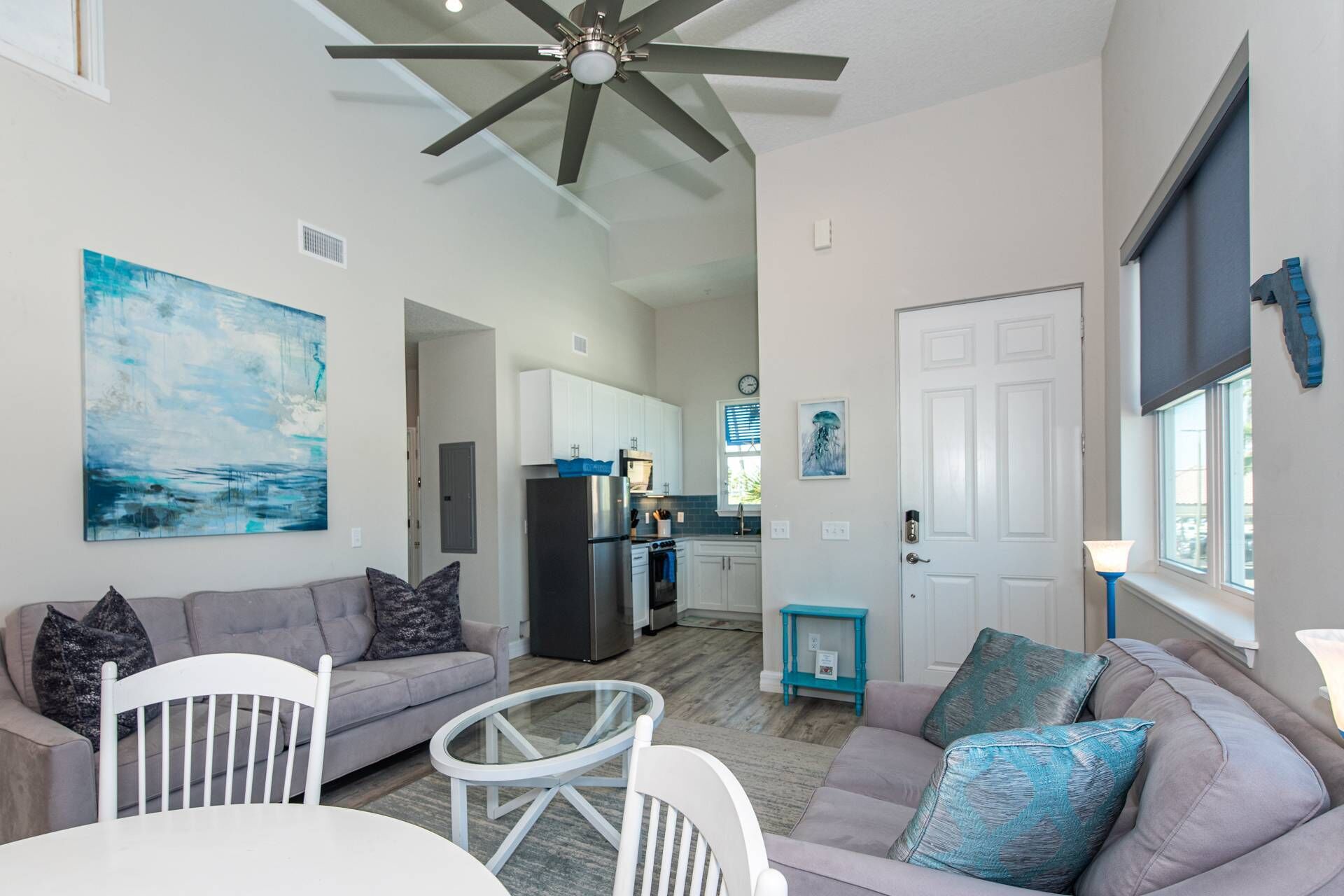 A modern living room with a gray sofa, a white dining table, and a ceiling fan.