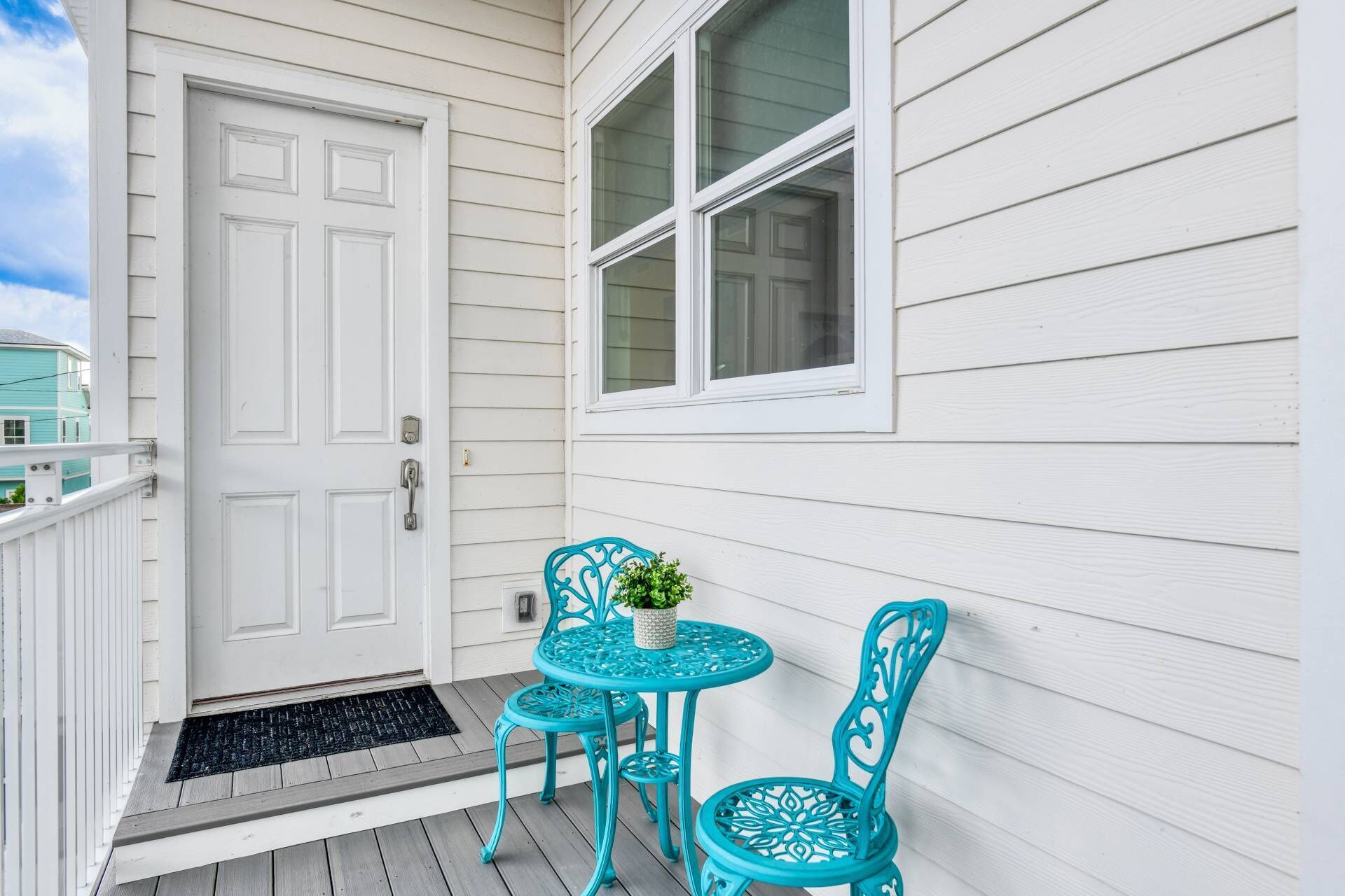 A porch with a white door, a window, and two turquoise chairs with a small table.