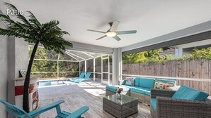 Une terrasse couverte, dotée de meubles en osier, d’un ventilateur de plafond et offrant une vue sur le jardin arrière.