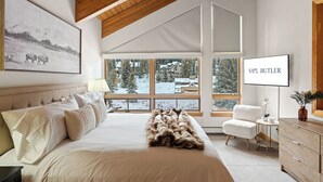 Quarto com uma cama grande, uma cadeira, uma televisão e uma janela com vista para a neve.