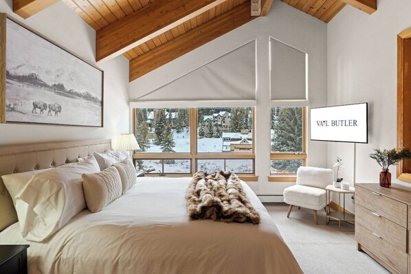 A bedroom with a large bed, a chair, a TV, and a window with a snowy view. - 122 West Meadow Drive (Vail)