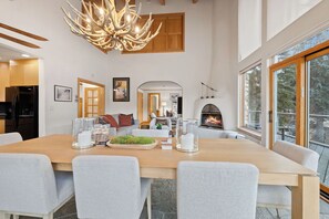 A modern dining area with a large wooden table, grey upholstered chairs, a chandelier, and a fireplace. - Beautiful riverside haven in the heart of Vail - walk to everything, sleeps 10 (Vail)
