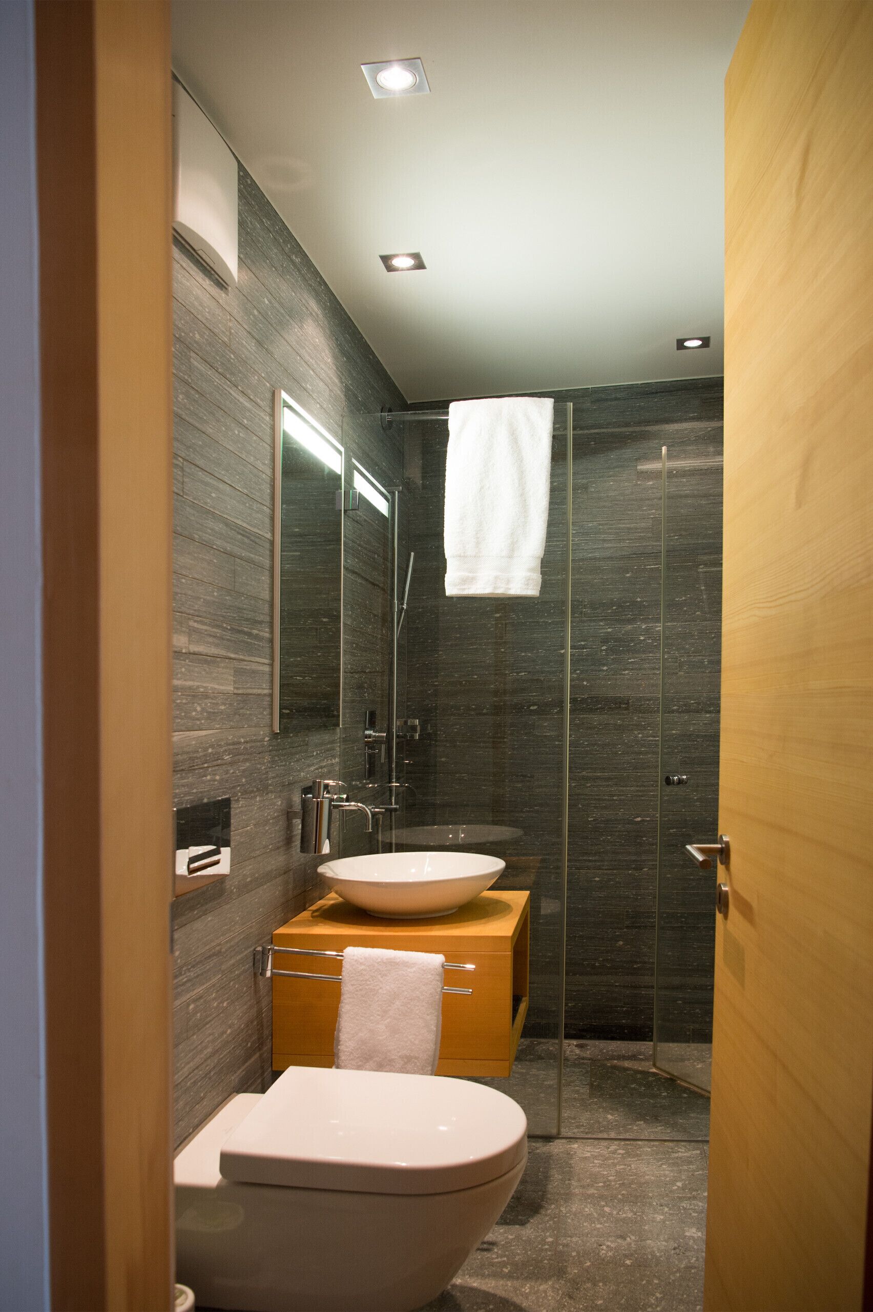 Ein modernes Badezimmer mit einer Glasdusche, einem Holzkosmetikschrank und einer weißen Toilette.