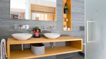 A modern bathroom with two large white sinks, a mirror, and a wooden vanity.