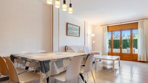 Een eetgedeelte met een tafel gedekt voor vier personen, witte stoelen en een schilderij aan de muur.