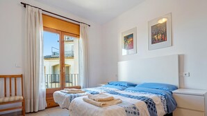 Een slaapkamer met een bed, twee nachtkastjes, een stoel en een balkon met gordijnen.