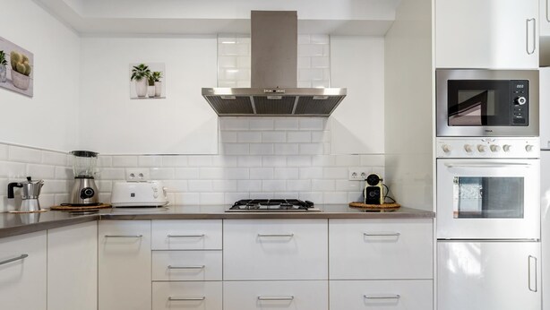 Een moderne keuken met witte kasten, een roestvrijstalen afzuigkap, een ingebouwde magnetron en een gasfornuis.