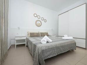 A modern bedroom with a large bed, a nightstand, a dresser, and a wardrobe.